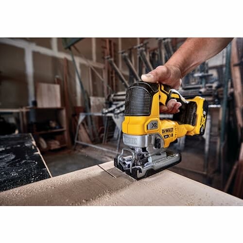 Person using a yellow cordless jigsaw to cut wood in a workshop.