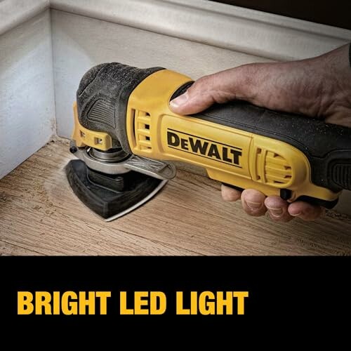 Hand holding DeWalt oscillating tool on wood surface with bright LED light.