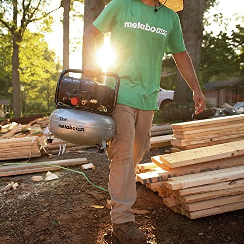 Person carrying a Metabo HPT air compressor at a lumber site.